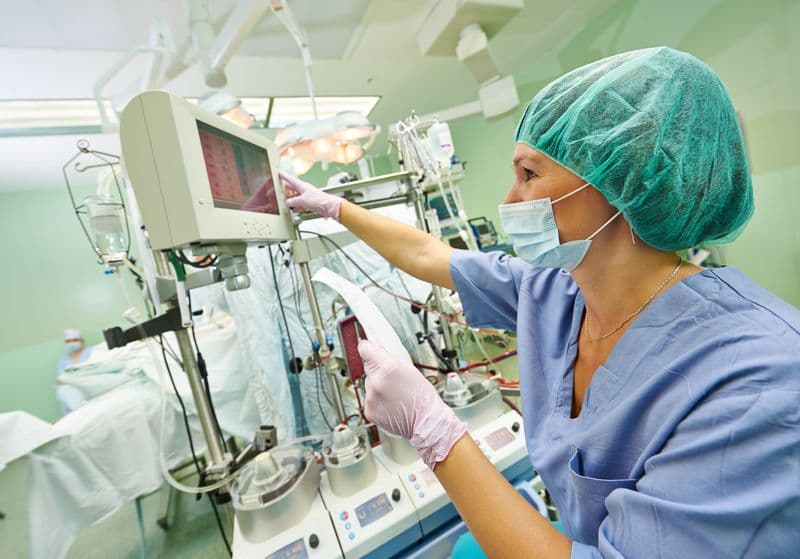 A nurse is looking at results on a machine and holding a piece of paper with medical information.