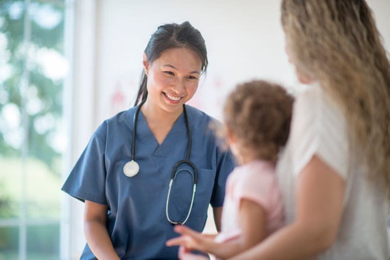 A nurse is smiling and talking to a small child and their mother.