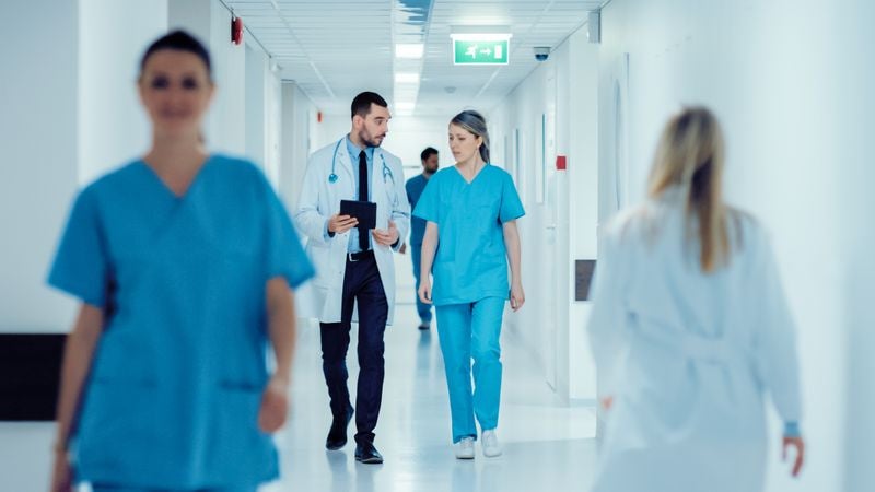 A doctor and nurse have an important discussion as they walk down a hallway in a hospital.
