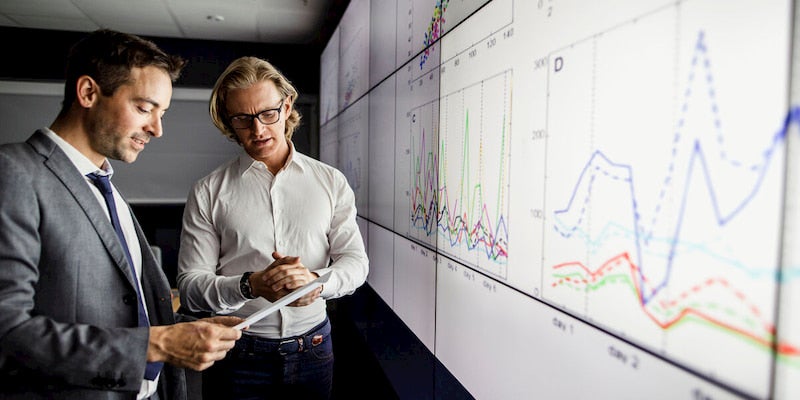 Two business consultants are standing next to a large graph discussing documents. 