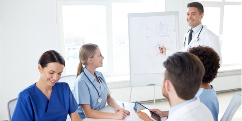 Group of happy nurses with mentor meeting and drawing on flip board at hospital