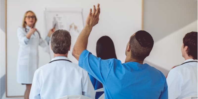 A nursing student in a lecture hall raises their hand to ask a question