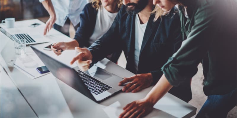 Professionals who work at a startup huddling together around a laptop to discuss business.