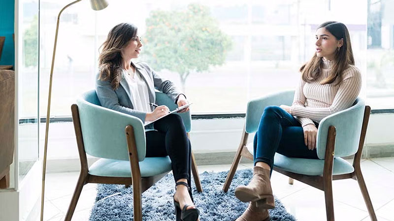 Two women having a counselling session in a bright room, with one taking notes.
