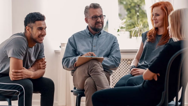 A group therapy session with a counselor and patients engaging in conversation.