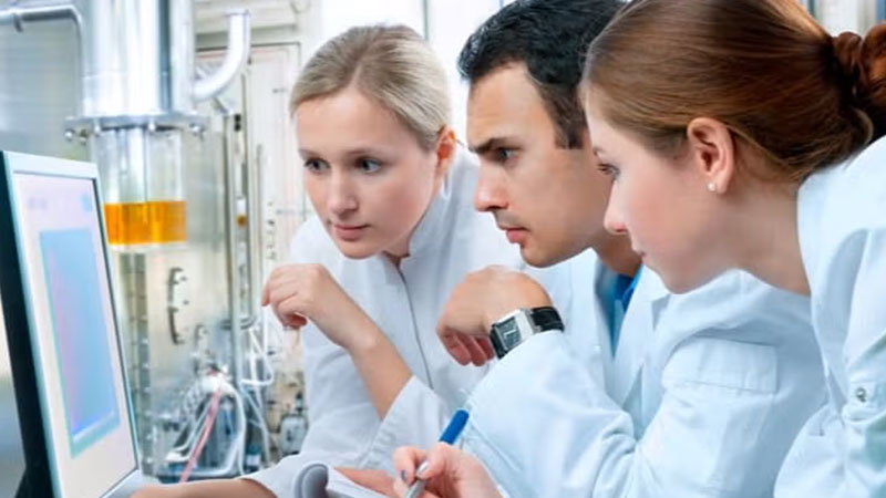 Three researchers analyzing data on a computer in a lab setting.