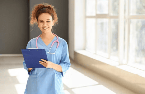 A smiling nursing student in blue scrubs standing confidently in a hallway.