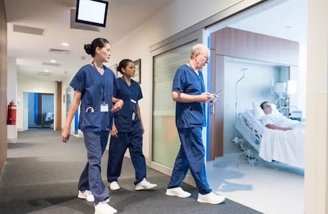 A group of nurses in blue scrubs walking through a hospital corridor.