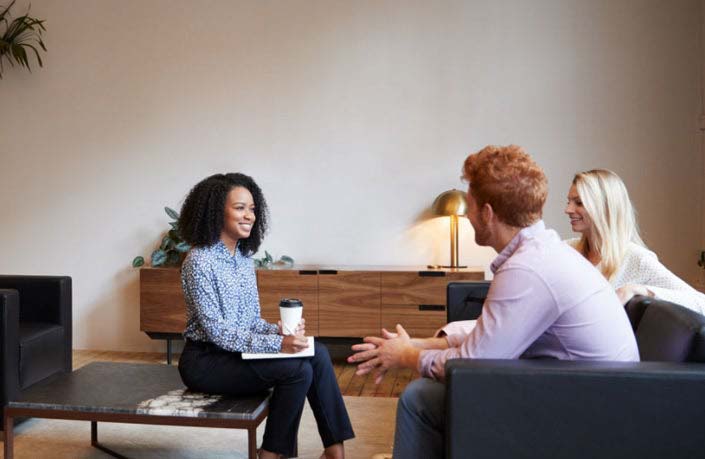 A therapist holding a coffee cup while talking to a smiling couple.
