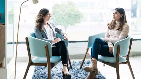 Two women having a counselling session in a bright room, with one taking notes.